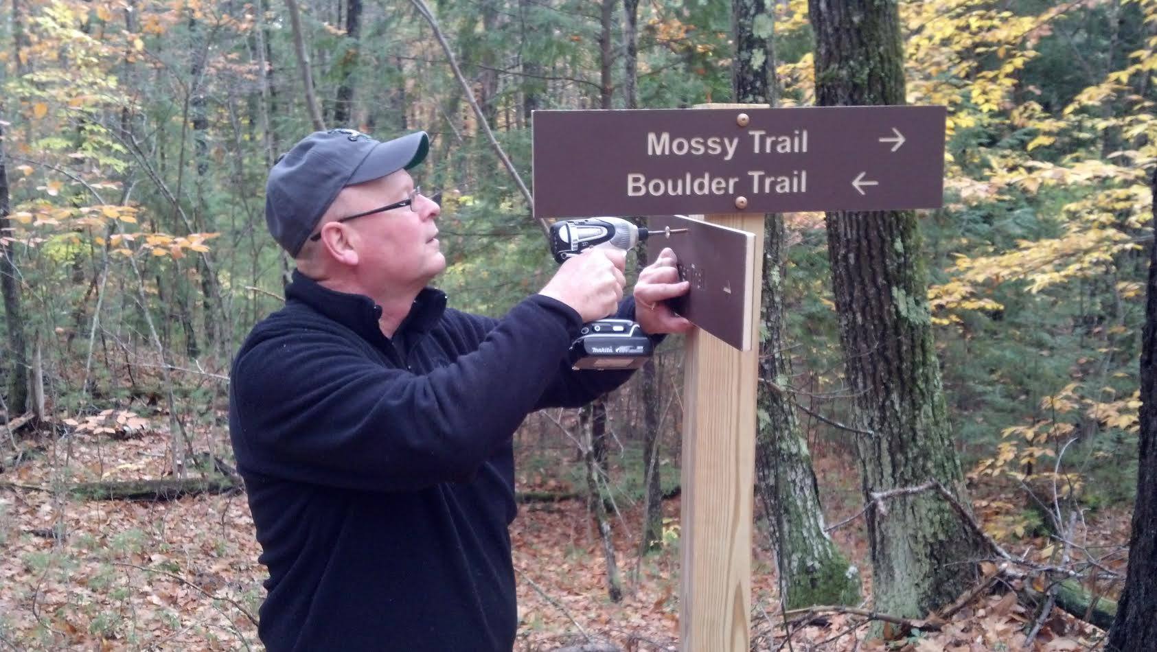 Man using to drill to hang up signs in the forest.